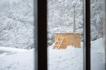 Wooden hot vat on snowy terrace at mountains. Winter vacation concept with hot bath outside