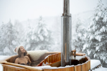 Woman relaxing in hot bath outdoors, enjoying thermal spa at snowy mountains. Winter holidays in...