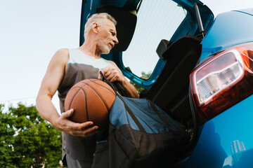 Grey senior sportsman getting ball out of bag in trunk