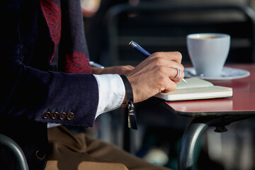 Close up of a business man writing in agenda sitting on a terrace bar. Business work concept
