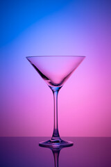 Empty martini glass on a pink and blue neon background. Alcohol drink, cocktail party concept....