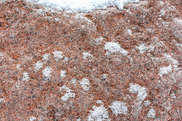 The red granite block was covered with frost on a cloudy day. The pattern and texture of stone and snow.