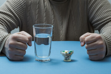 On the table in front of the man is a glass of water and medicines. The man has a tragedy.