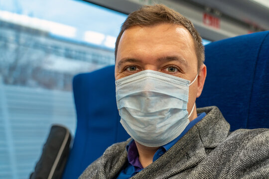 Portrait of male passenger wearing medical face mask in public transportation. Millennial man looking at camera, thinking, going to home by train during coronavirus pandemic. New normal