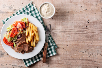 Plate of kebab, vegetables and french fries on wooden table. Top view. Copy space