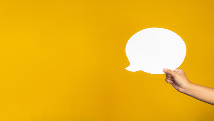 A speech bubble concept. Hand holding of an empty white speech balloon on yellow background. - obrazy, fototapety, plakaty