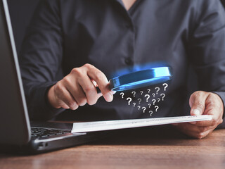 A businessman is holding a magnifying glass looking at a question mark symbol on a document while sitting in the office.