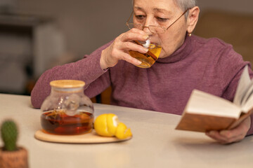 Fototapeta premium woman sitting at the table drinking tea with lemon and reading a book