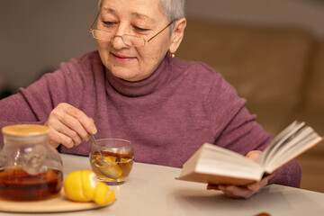 woman sitting at the table drinking tea with lemon and reading a book