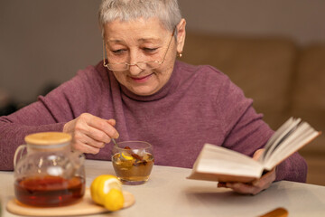 woman sitting at the table drinking tea with lemon and reading a book