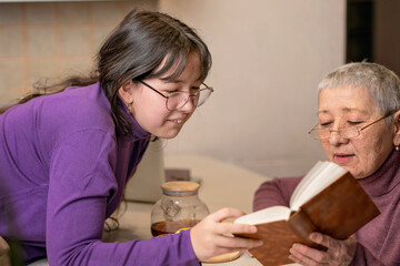 grandmother and granddaughter drink tea sitting at the table and read a book.
