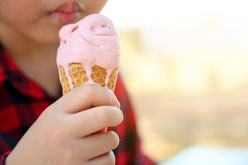 Close up hand of asian boy holding sweet strawberry ice cream in a wafer cone, concept of happy childhood, child 6-year-old boy enjoy with his ice-cream.