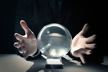 Businessman using crystal ball to predict future at table in darkness, closeup - obrazy, fototapety, plakaty