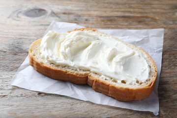 Slice of bread with tasty cream cheese on wooden table, closeup