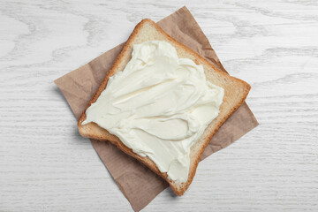 Slice of bread with tasty cream cheese on white wooden table, top view