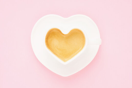 Coffee in heart shape mug on a light pink background. Valentine's day concept. Top view, copy space