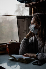 A young woman in medical mask is traveling by train alone. Taking precautions