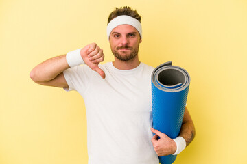 Young sport caucasian man going to yoga classes while holding a mat isolated on yellow background...