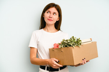 Young English woman making a move while picking up a box full of things isolated on blue background dreaming of achieving goals and purposes