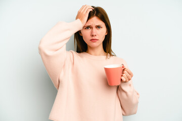 Young English woman holding a mug isolated on blue background being shocked, she has remembered...