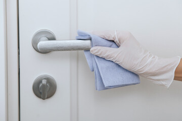 Cleaning door handle with blue wipe in white gloves. Woman hand using towel for cleaning home room door link. Sanitize surfaces prevention in hospital and public spaces against corona virus.