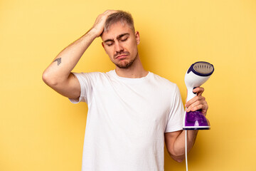 Young caucasian man holding an iron isolated on yellow background being shocked, she has remembered...