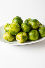 View of green Brussels sprouts on white plate, white background, vertical, with copy space