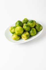 Top view of green Brussels sprouts on white plate, white background, vertical, with copy space