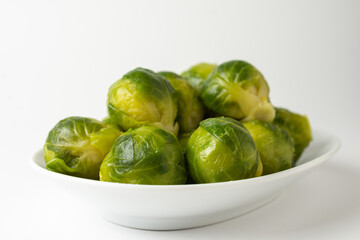 Close-up of green Brussels sprouts on a white plate, white background, horizontal, with copy space