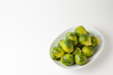 Top view of a group of green Brussels sprouts on a white plate, white background, horizontal, with copy space