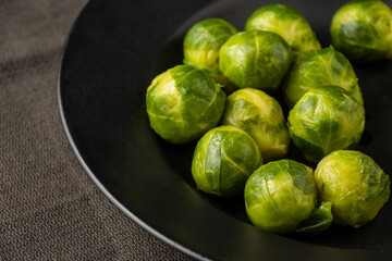 Top view of frozen brussels sprouts on black plate and dark cloth, selective focus, horizontal