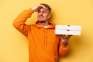 Young caucasian man holding pizzas isolated on yellow background being shocked, she has remembered...
