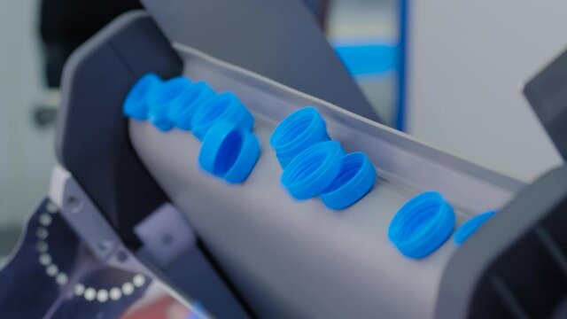 Many blue plastic bottle caps falling from conveyor belt at factory, exhibition - production line. Manufacturing, industry, recycling and technology equipment concept