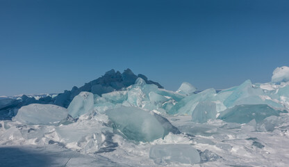 A block of turquoise ice hummocks on a frozen lake. Sun glare on the edges. Shadows on the snow....