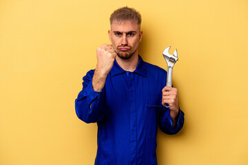 Young electrician caucasian man isolated on yellow background showing fist to camera, aggressive...