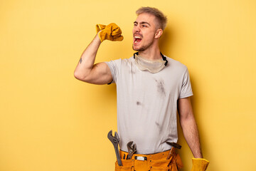 Young electrician caucasian man isolated on yellow background raising fist after a victory, winner...