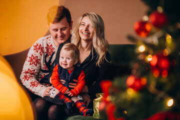 Young family with baby girl sitting by Christmas tree