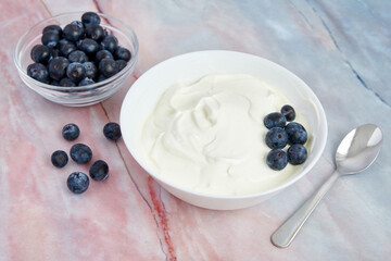 Bowl with Greek yogurt and blueberries on a marble background