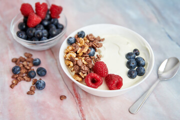 Bowl with Greek yogurt, nuts, cereals, blueberries and fresh raspberries on a marble background