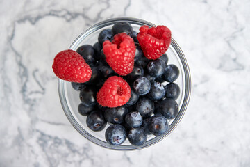 Bowl with blueberries and fresh raspberries on a marble background