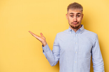 Young caucasian man isolated on yellow background showing a copy space on a palm and holding...