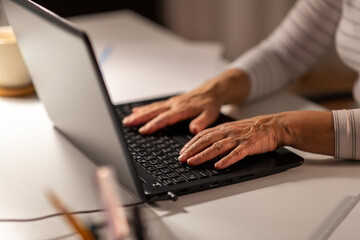 technology and people concept - close up of senior woman hands typing on laptop at home