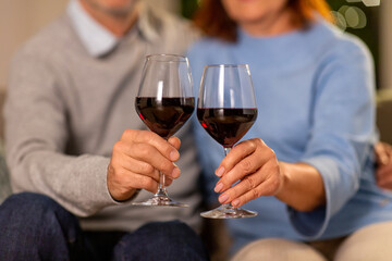 holidays, drinks and people concept - close up of senior couple toasting glasses of red wine at home in evening
