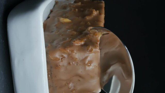 vertical screen orientation, Dolly shot, shiny steel spoon breaks off a piece of chocolate mousse cake on white ceramic substrate