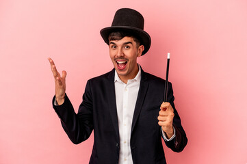 Young caucasian wizard man holding a wand isolated on pink background receiving a pleasant...
