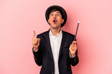 Young caucasian wizard man holding a wand isolated on pink background pointing upside with opened...