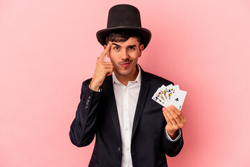 Young caucasian wizard man holding a magic cards isolated on white background pointing temple with...