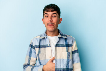 Young mixed race man isolated on blue background touches tummy, smiles gently, eating and satisfaction concept.