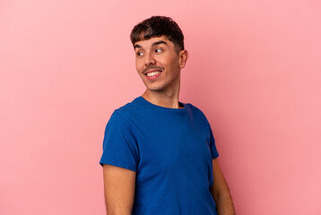 Young mixed race man isolated on pink background looks aside smiling, cheerful and pleasant.