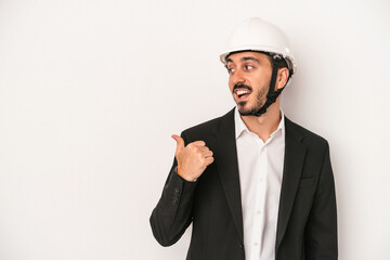 Young architect man wearing a construction helmet isolated on white background points with thumb finger away, laughing and carefree.